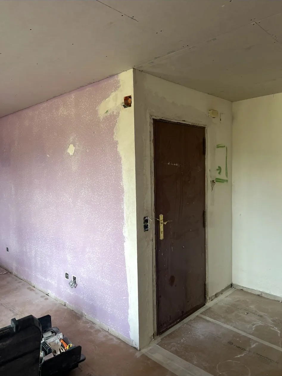 Entrada de un piso en obra con la pared lila y gotelé, la puerta de madera y el suelo cubierto con cartón de protección