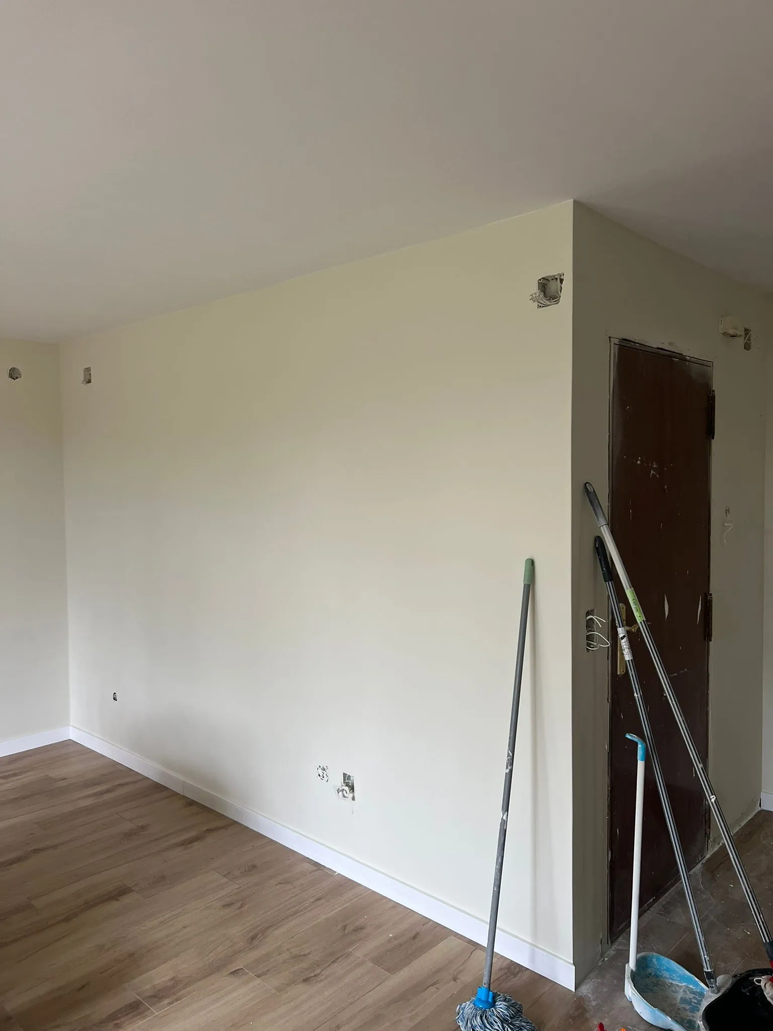 La misma entrada terminada, con las paredes lisas en tono crema, rodapié blanco y suelo laminado de madera
